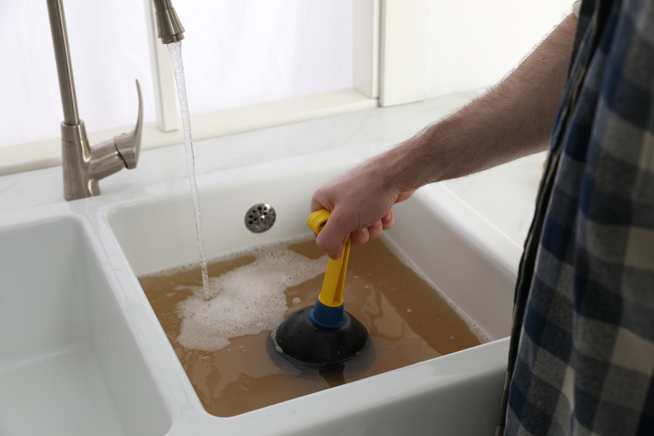 Man Using Plunger to Unclog Sink Drain in Kitchen, Closeup