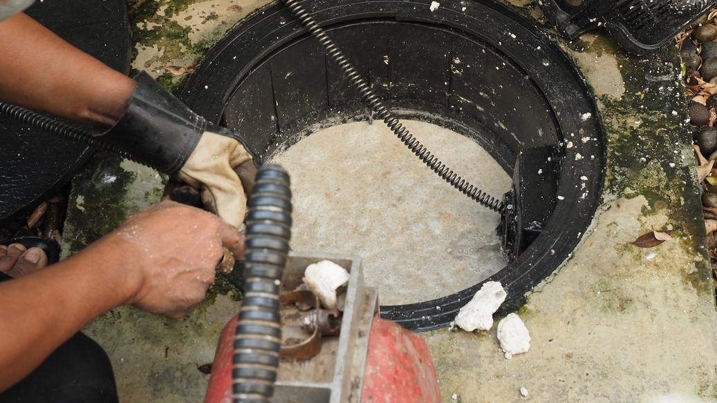 Plumber Repairing Clogged Grease Trap with Auger Machine